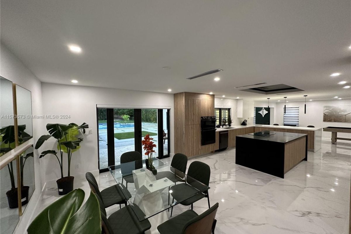 A dining area and kitchen with house plants, a glass dining area surrounded by chairs, and an island with countertops.