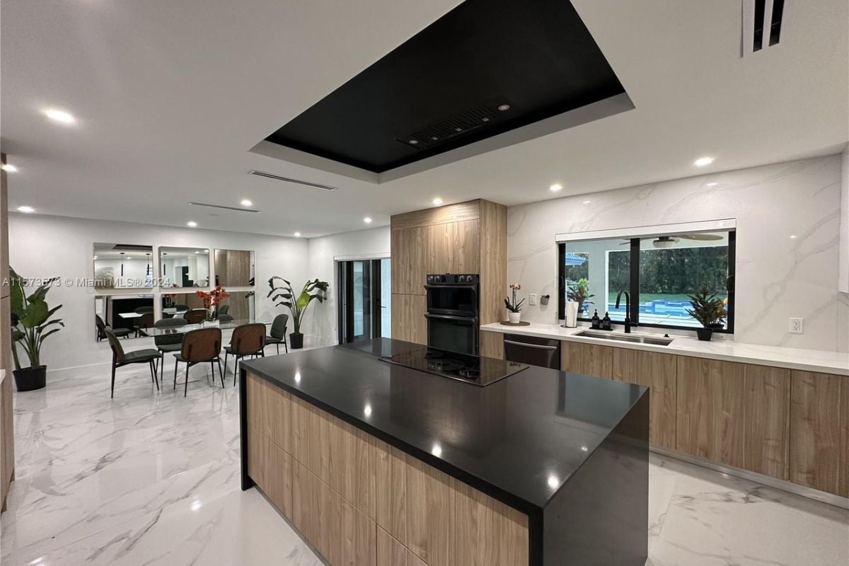 A dining area and kitchen with house plants, a glass dining area surrounded by chairs, and an island with countertops.