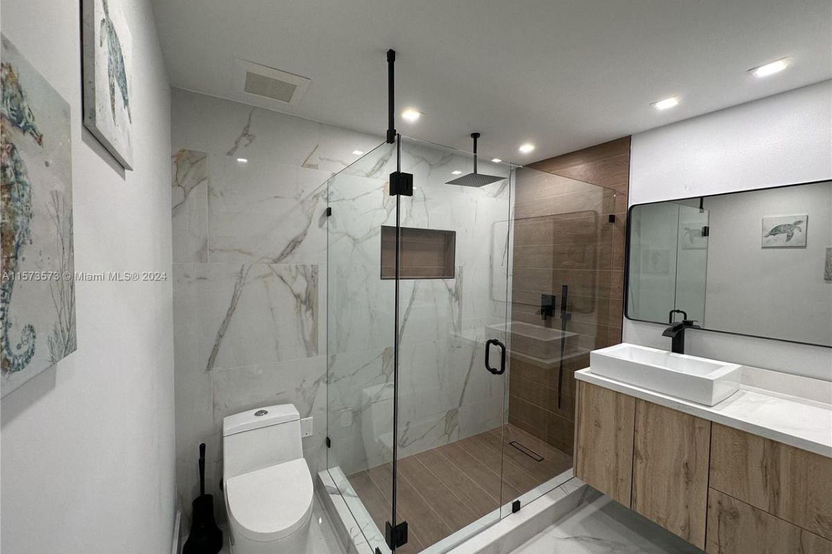 A bathroom with a vanity, mirror, cabinets, shower room, and toilet.