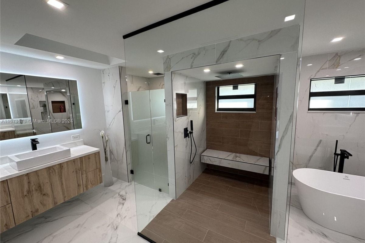 A bathroom with a vanity, mirror, cabinets, shower room, and bathtub.