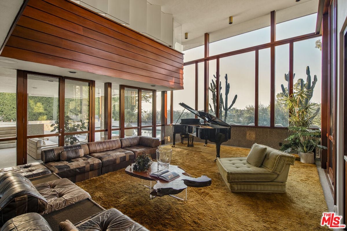 A living room with a rug, houseplants, couches, tall windows, and a coffee table.