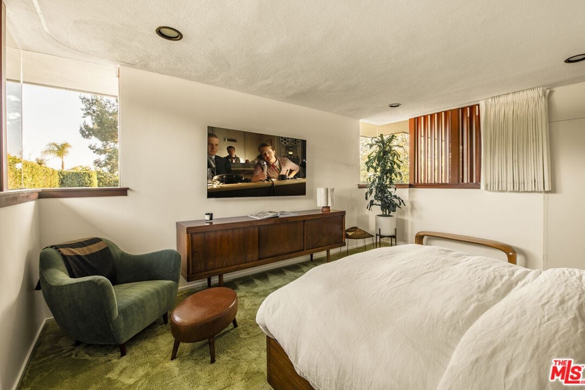 A bedroom with a bed, window, nightstand, plant, TV, studio couch, and cabinet.