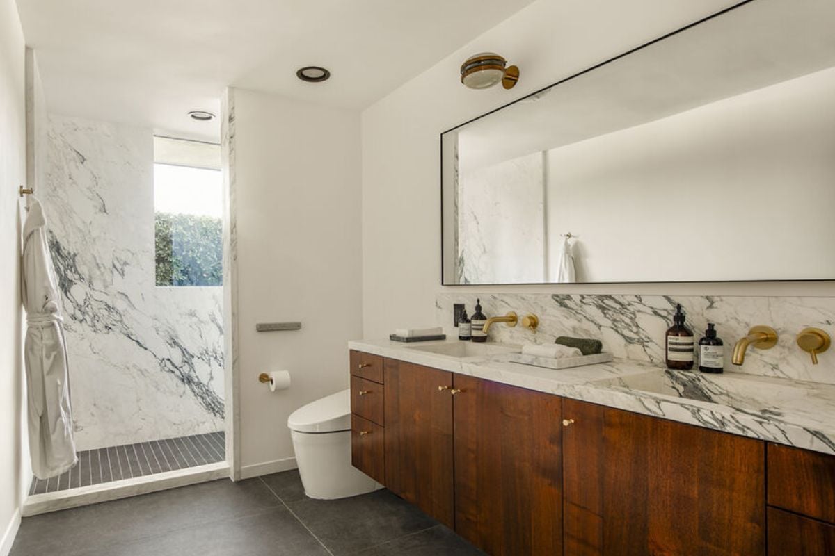 A bathroom with a countertop, mirror, sink, cabinets, and toilet.