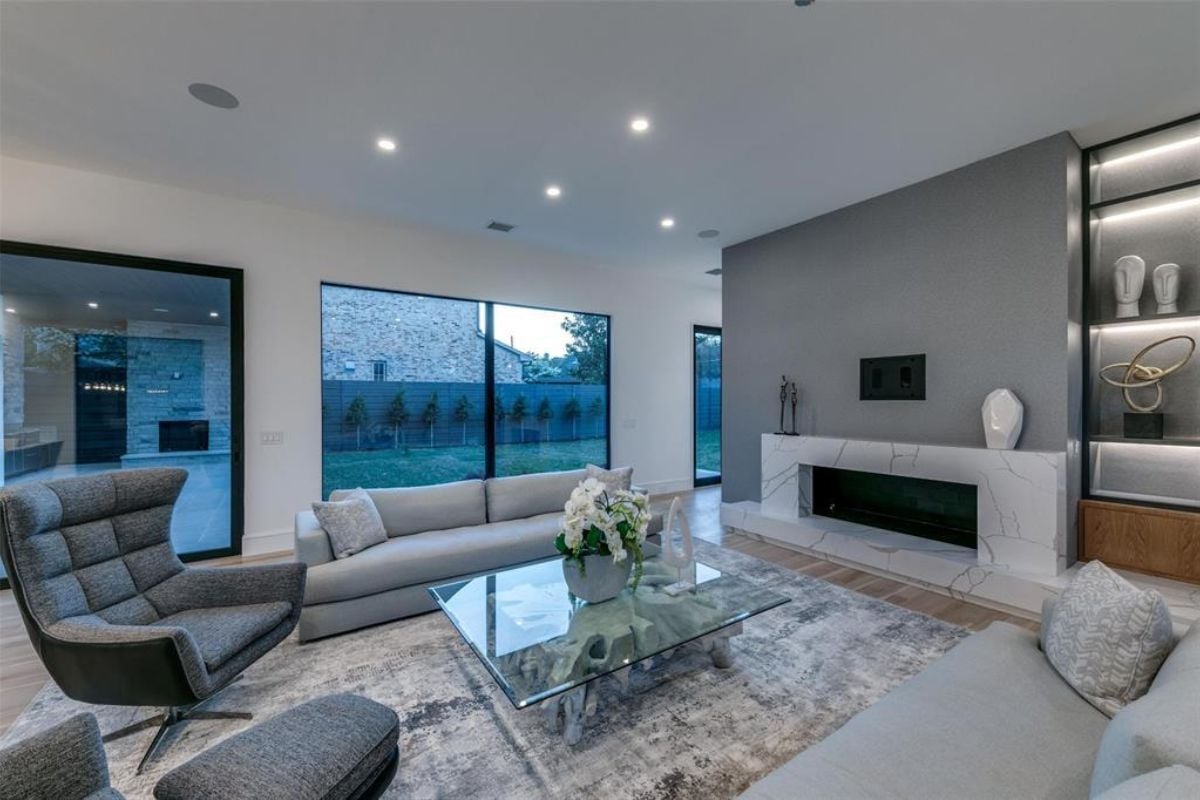 A living room with a fireplace, windows, couches, chairs, and a glass center table.
