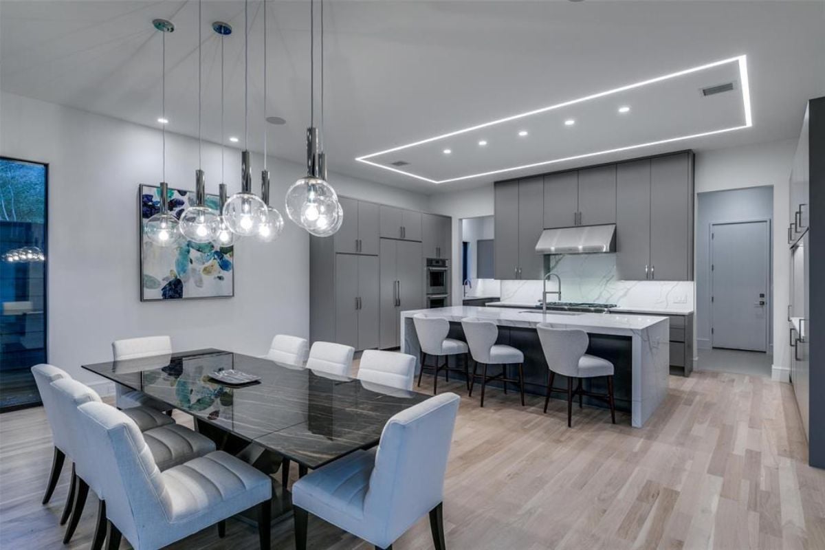 A dining area and kitchen with a dining table surrounded by chairs, countertops, sink, and cabinets.