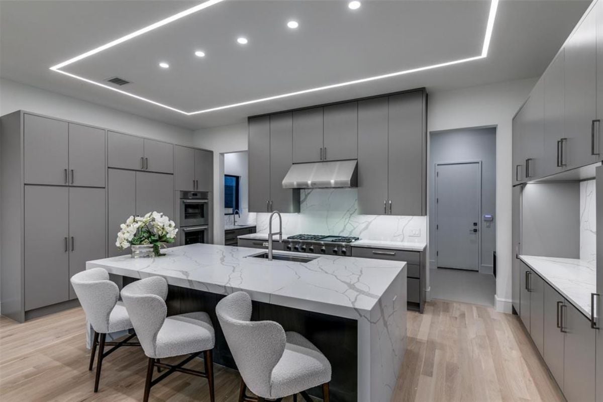 A kitchen with an island, chairs, sink, cabinets, and stove.