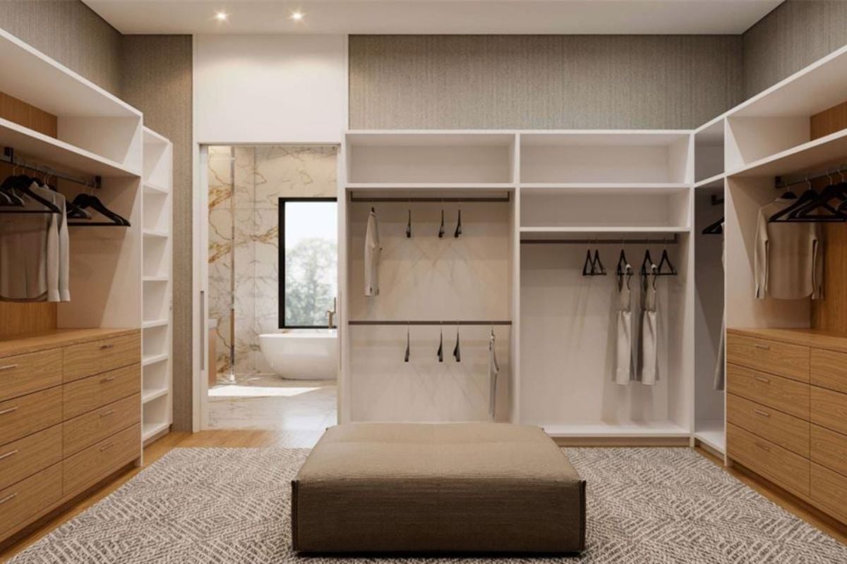 A walk-in closet with cabinets and an ottoman.