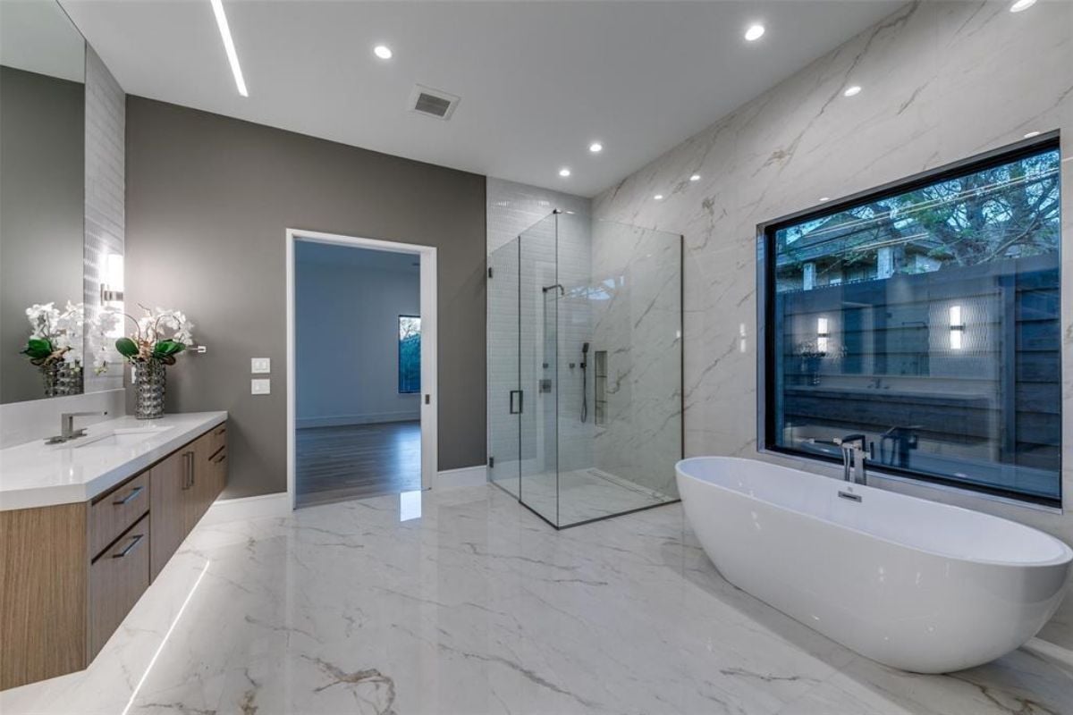 A bathroom with marble walls, marble floors, a countertop, sink, cabinets, and a bathtub.