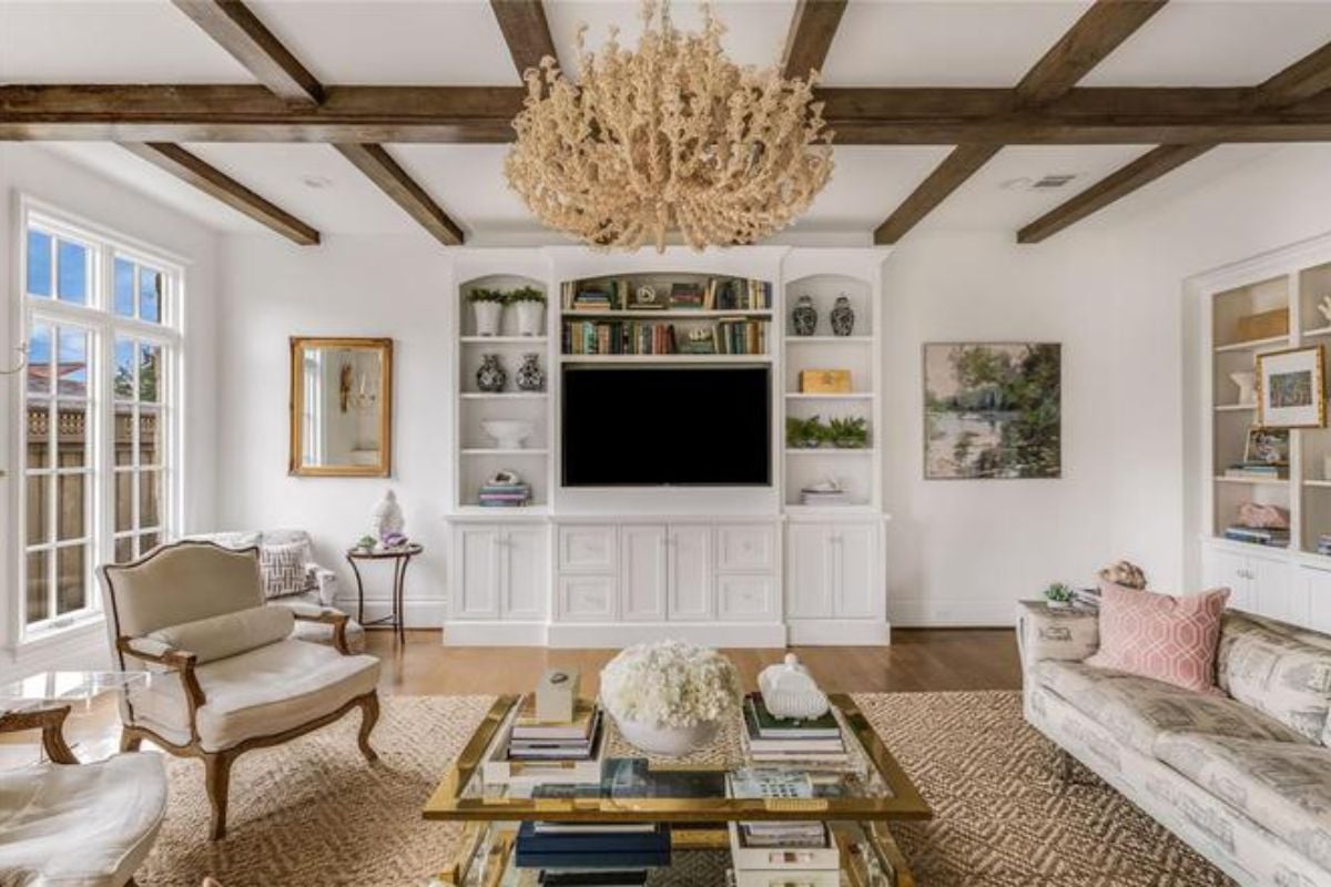 A living room with an exposed beam ceiling, chandelier, shelves, cabinets, couch, chair, and center table.