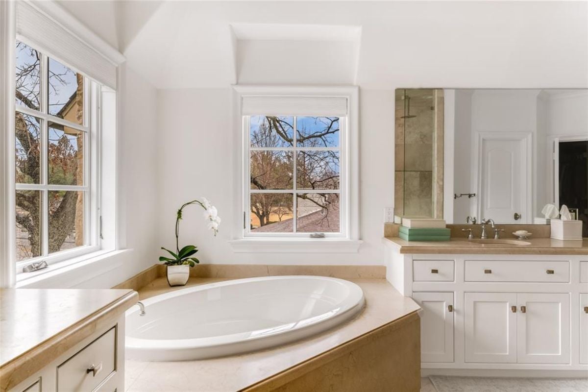 A bathroom with a vanity, mirror, cabinets, and bathtub.