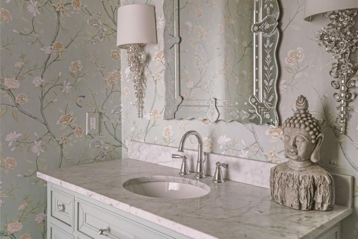 A bathroom with a vanity, wallpaper, and a mirror.