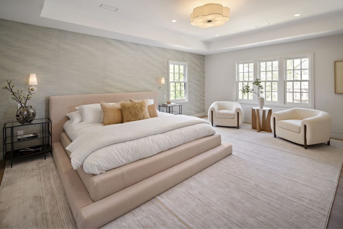 A bedroom with a bed, side table, vase, windows, and couches.
