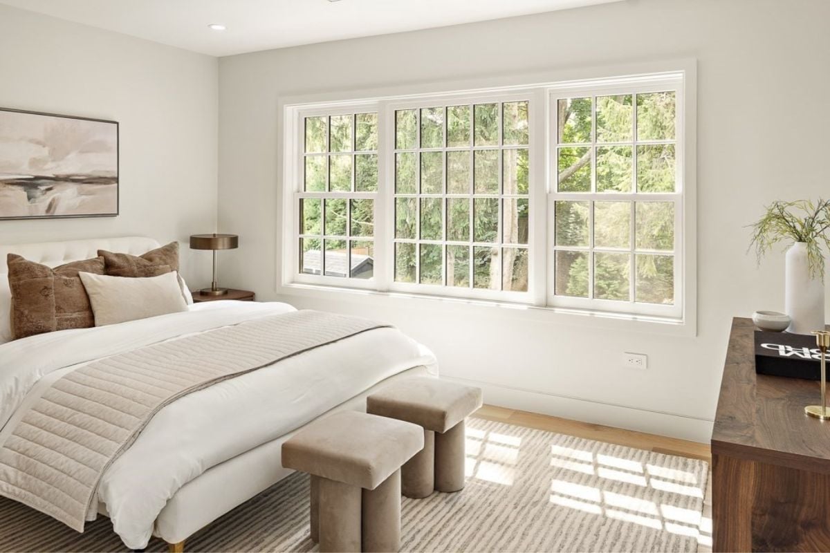 A bedroom with a bed, painting, windows, chairs, and cabinets.