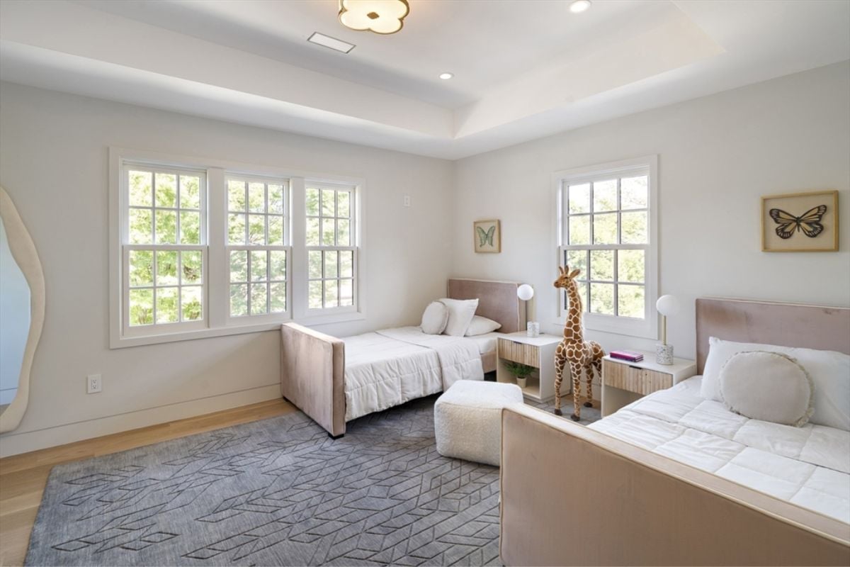 A bedroom with two beds, nightstands, windows, and a rug.