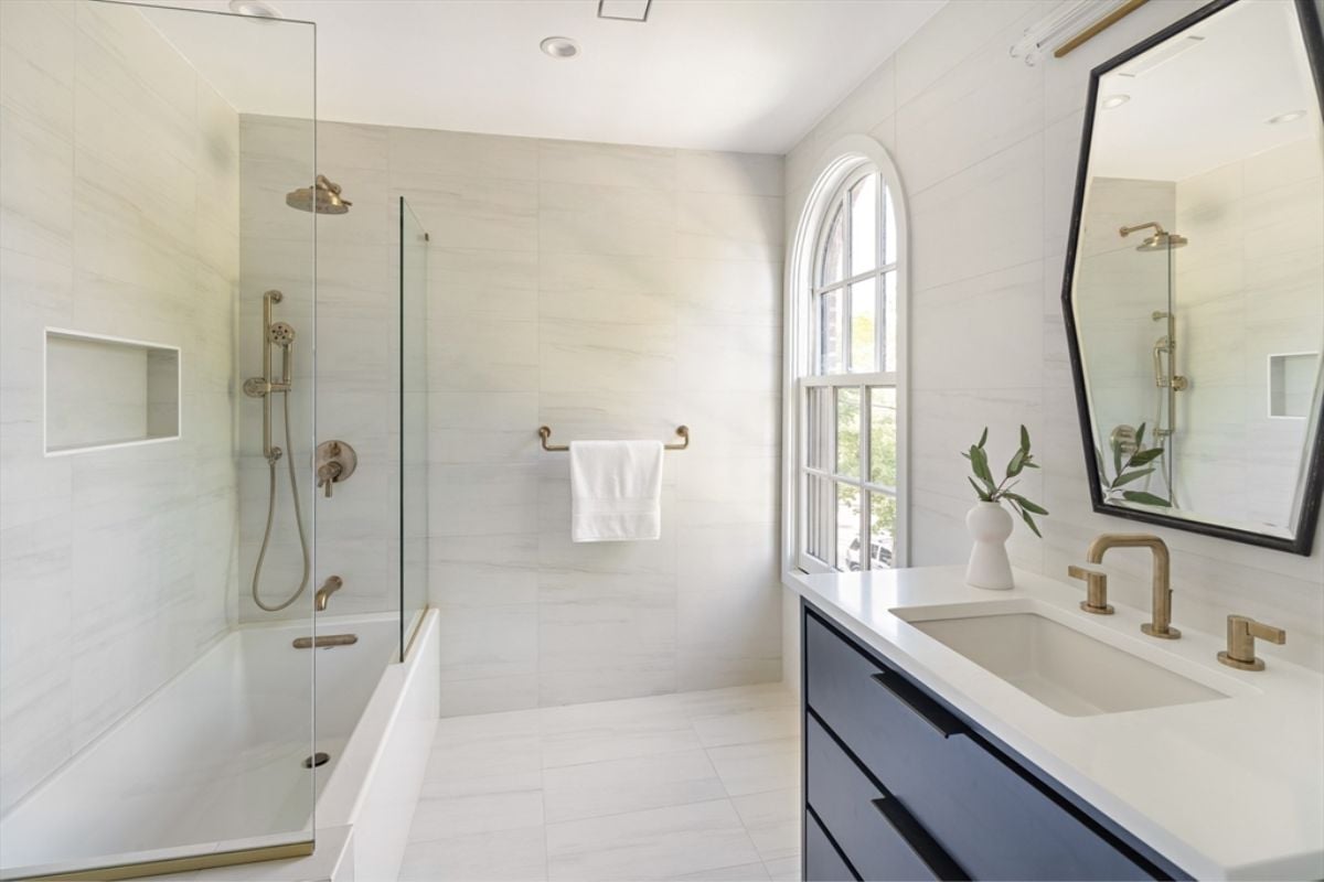 A bathroom with a vanity, cabinet, sink, mirror, window, tiled floor, and bathtub.