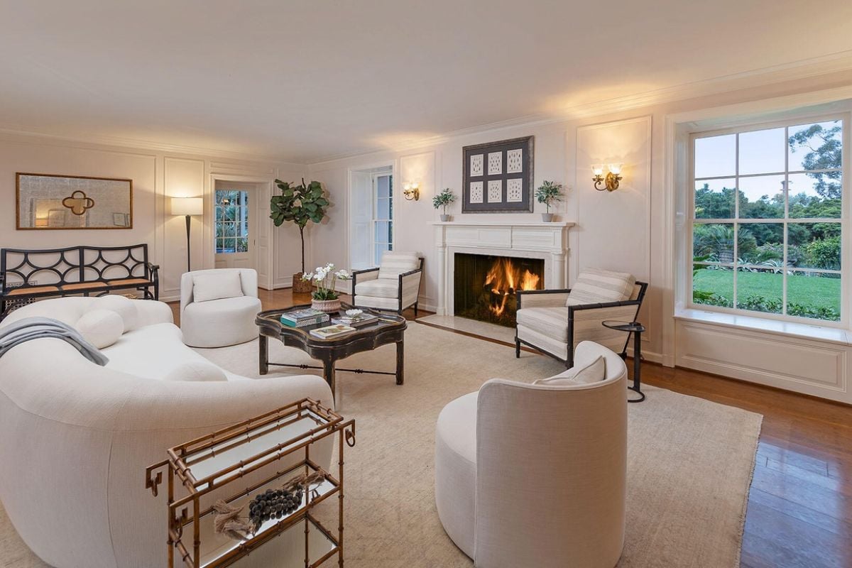 There is a living room with a rug, fireplace, windows, couch, chairs, and a center table.