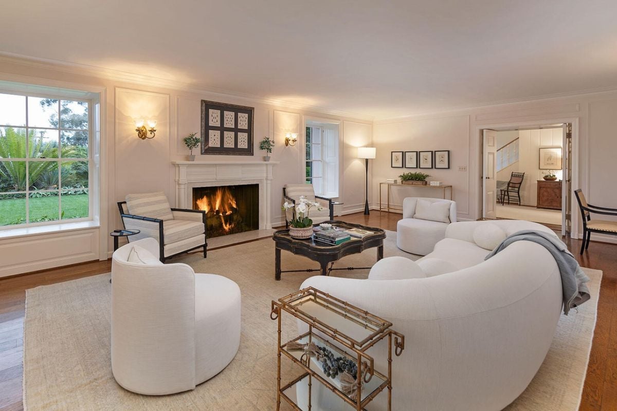 A living room with a rug, fireplace, windows, couch, chairs, and a center table.