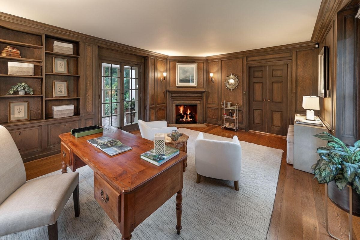 A home office with fireplace, shelf, rug, desk, and chairs.