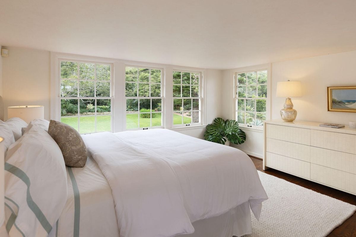 A bedroom with bed, windows, potted plant, and cabinet.