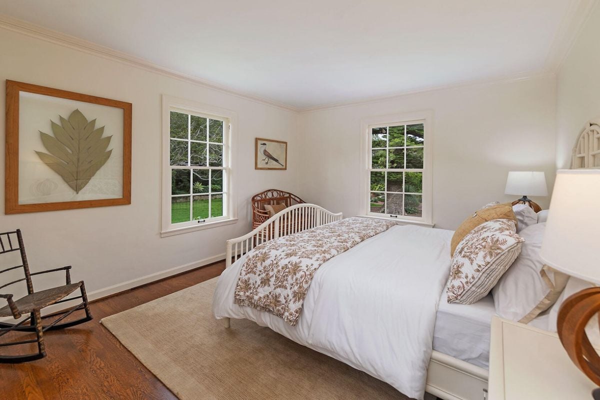 A bedroom with a bed, windows, nightstand, and chairs.