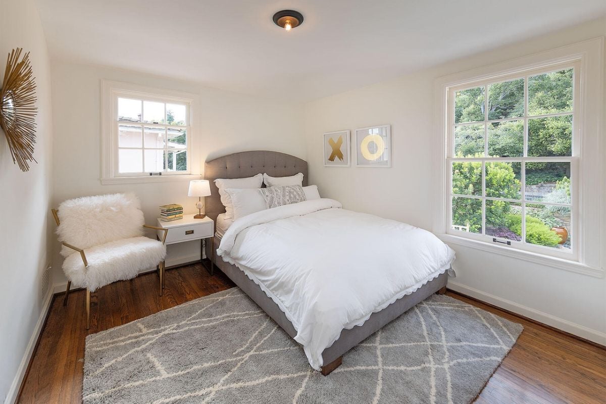 A bedroom with a bed, windows, nightstand, and chair.
