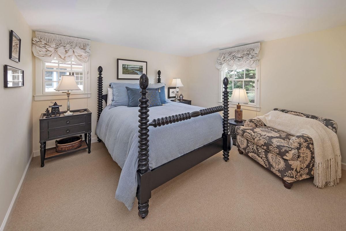 A bedroom with a bed, windows, nightstand, and couch.