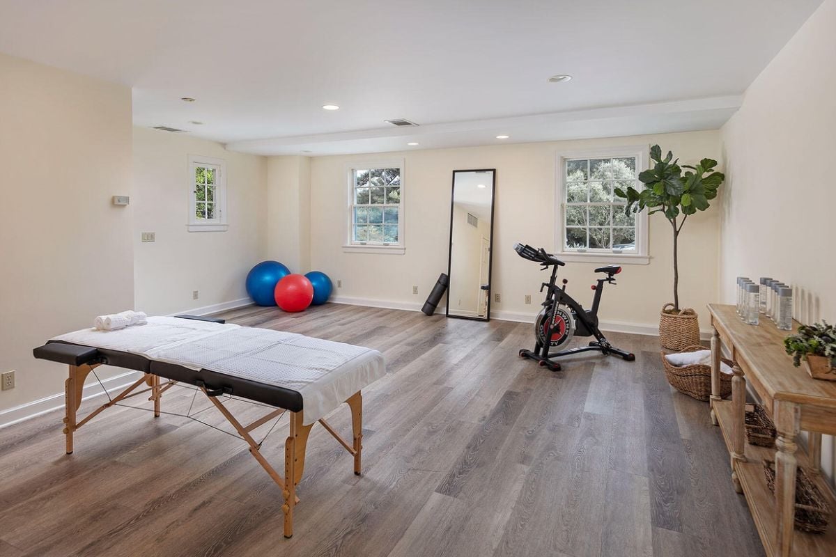 A massage room with a massage table, houseplants, and a stationary bike.