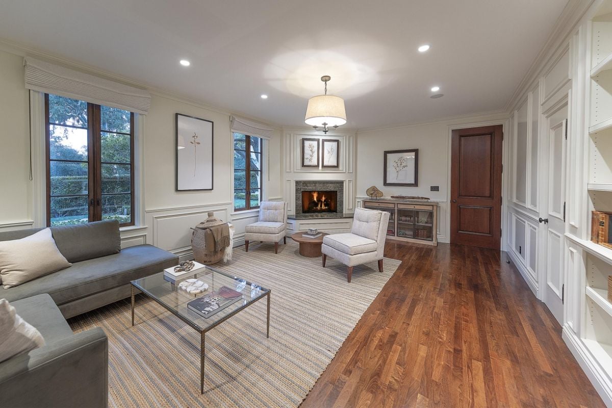 A living room with a fireplace, windows, couch, chairs, coffee table, cabinet, and shelf.