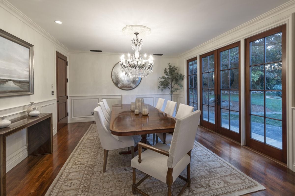 A dining room with a chandelier, painting, rug, and dining table surrounded by chairs.