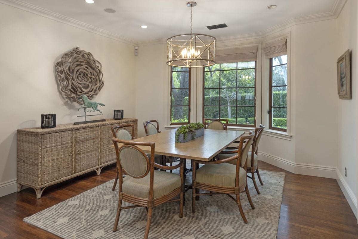 A dining room with a window, chandelier, cabinets, rug, and a dining table surrounded by chairs.