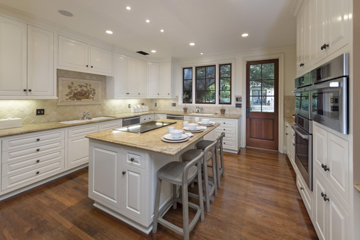 A kitchen with a center island, stools, countertop, sink, cabinets, and kitchen appliances.
