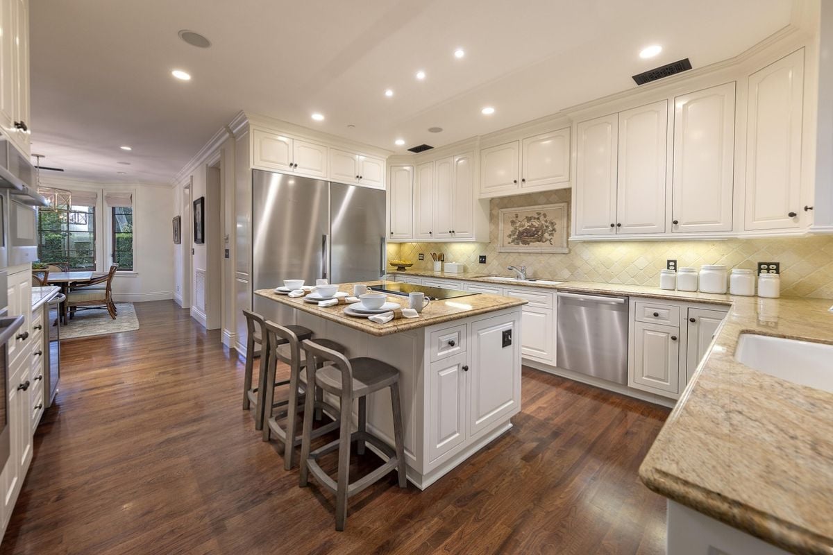 A kitchen with a center island, stools, countertop, sink, cabinets, and kitchen appliances.