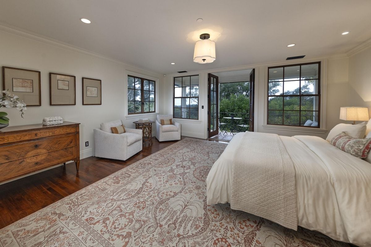 A bedroom with a bed, cabinet, single couches, coffee table, and windows.