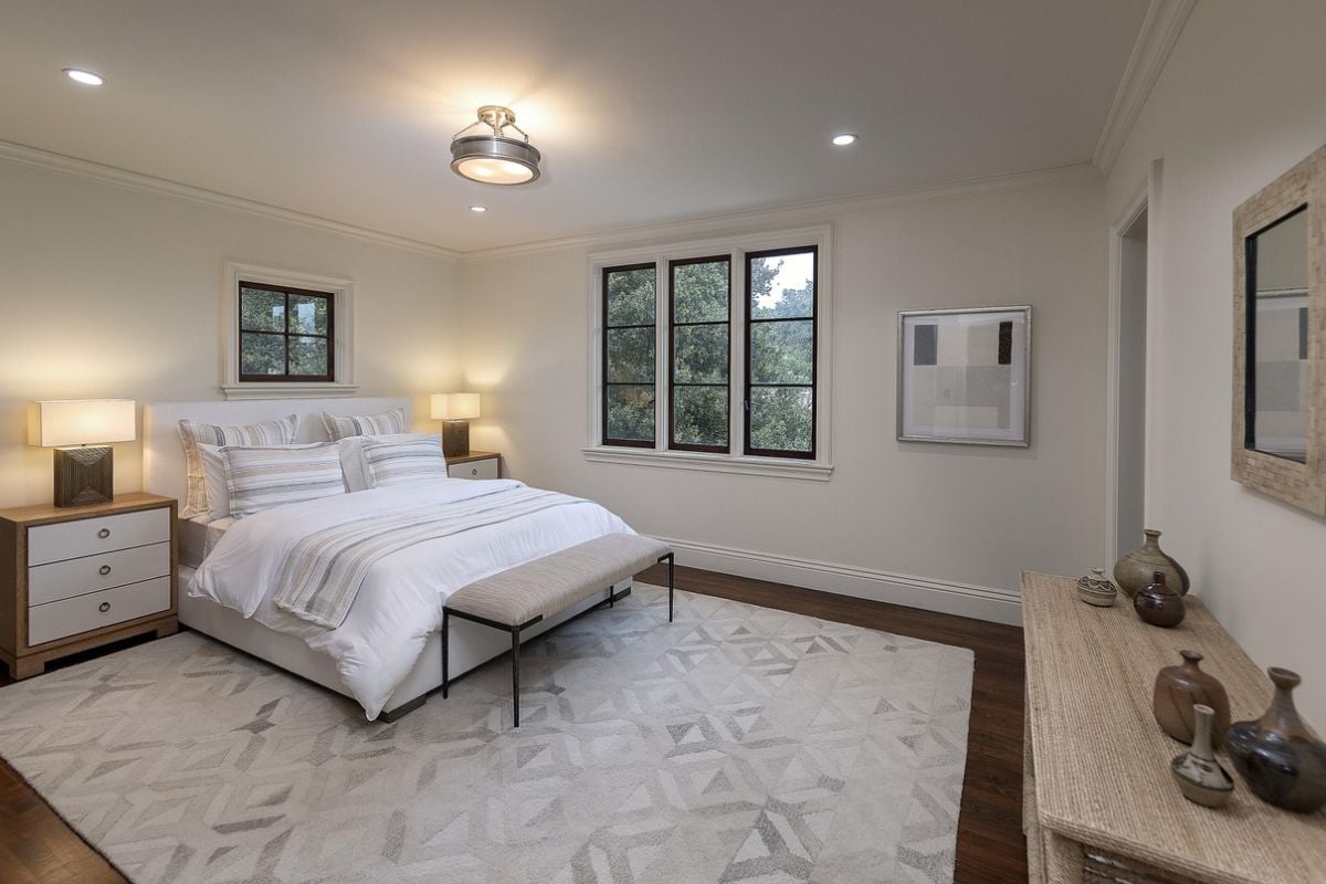 A bedroom with a bed, nightstand, windows, and lampshades.