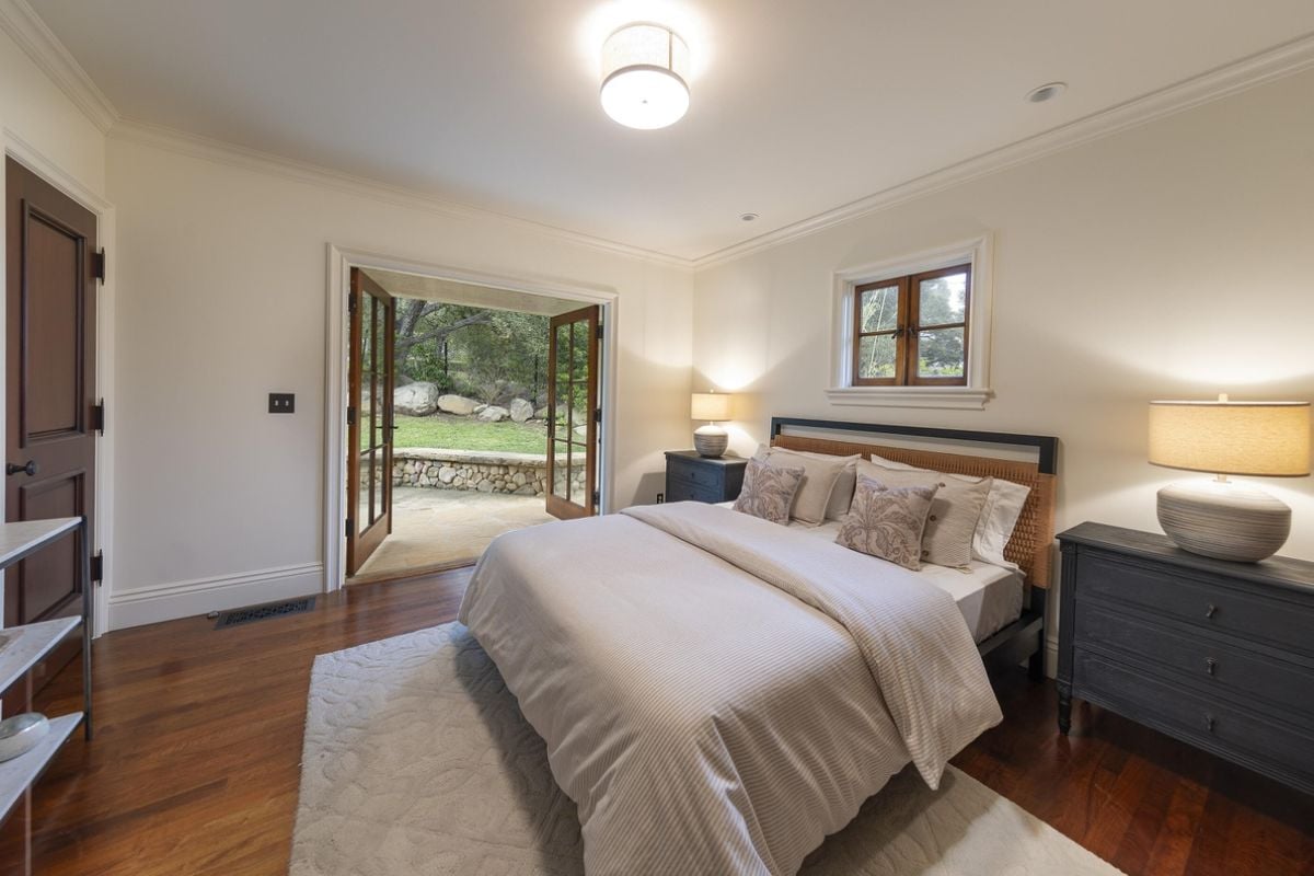 A bedroom with a bed, window, nightstand, and lampshades.
