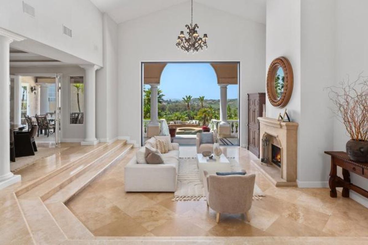 A living room with a fireplace, couches, chairs, a center table, a chandelier, and a vaulted ceiling.