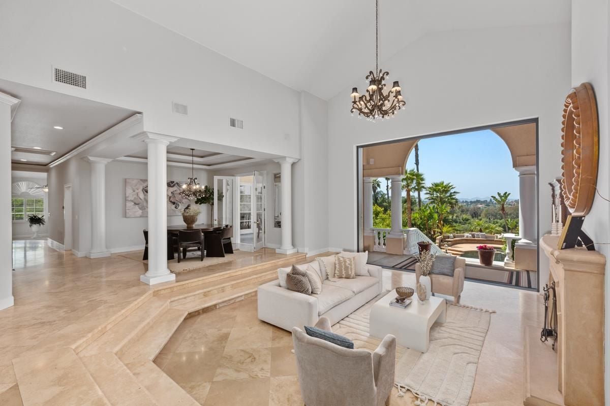 A living room with a fireplace, couches, chairs, a center table, a chandelier, and a vaulted ceiling.