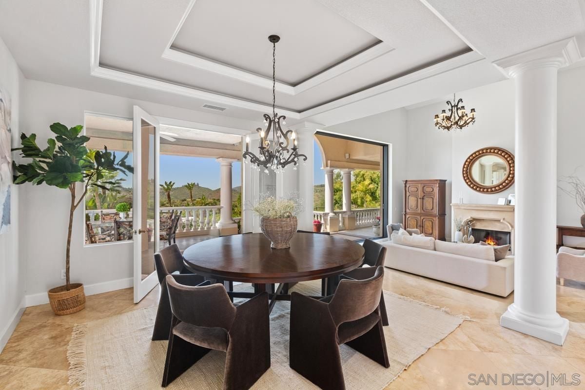 A dining area with plants, a chandelier, tiled floor, rug, and a round dining table surrounded by chairs.