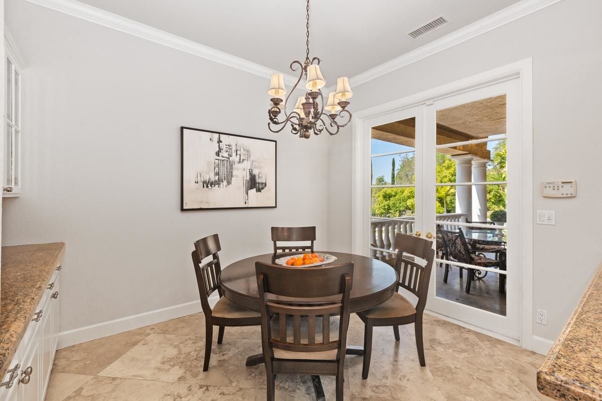 A breakfast nook with a chandelier, tiled floor, and a round table surrounded by chairs.
