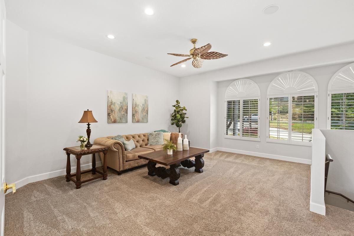 A loft with windows, a ceiling fan, a couch, and a center table.