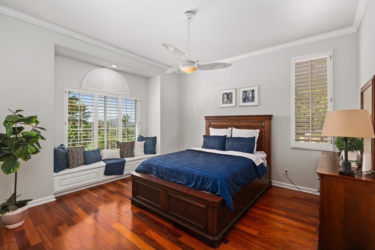 A bedroom with a bed, windows, ceiling fan, potted plant, and a window seat.