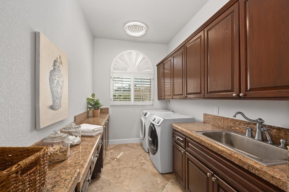 A laundry room with countertops, sink, cabinets, and washing machines.