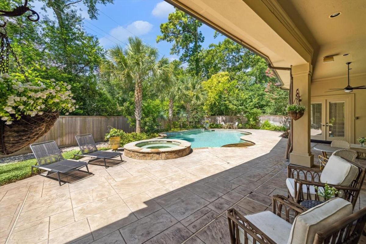 A patio with chairs and a swimming pool with a jacuzzi, surrounded by plants and trees.
