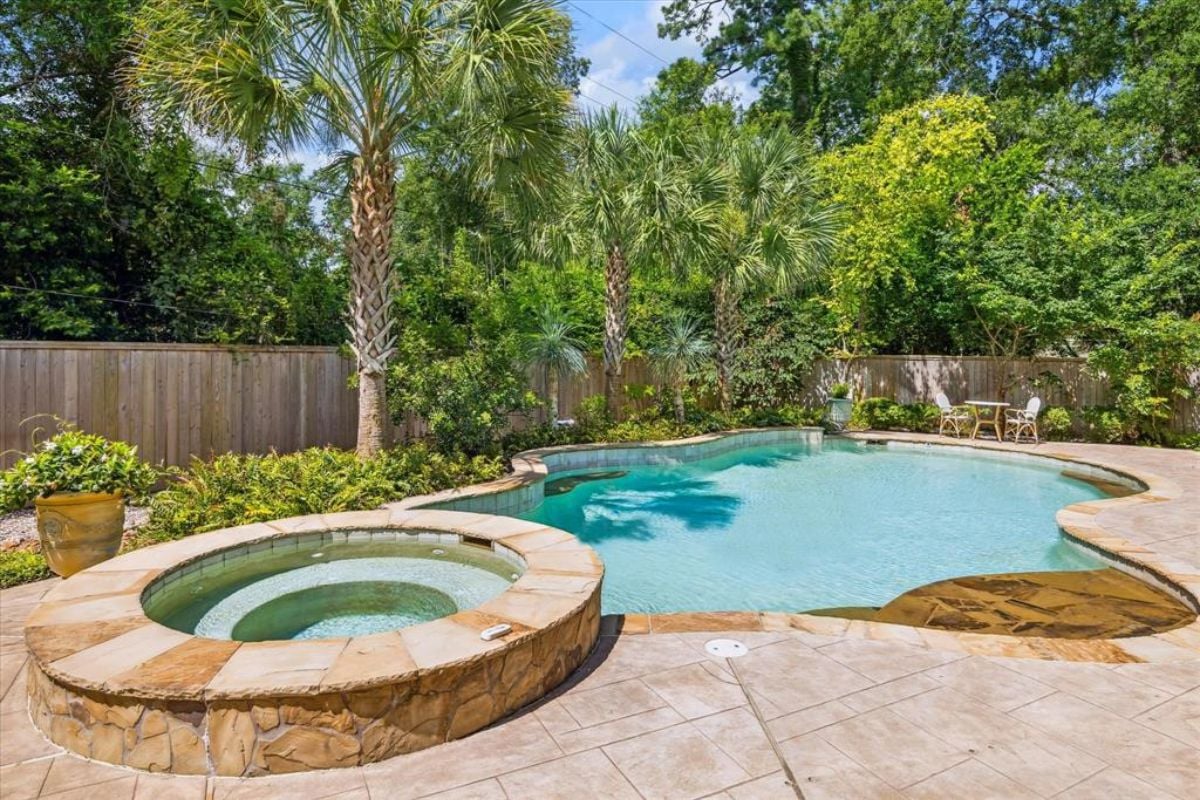 A swimming pool with a jacuzzi surrounded by plants and trees.