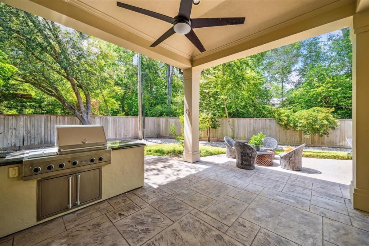 A patio with a griller, ceiling fan, and a table with chairs.