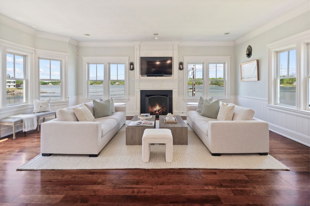 A sunroom with a TV, fireplace, white couches, a center table, and windows.