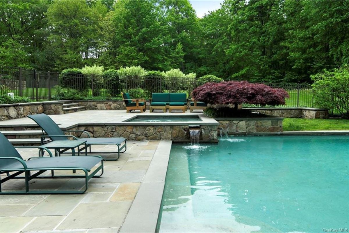 A swimming pool with a Jacuzzi, surrounded by plants and chairs on the poolside.