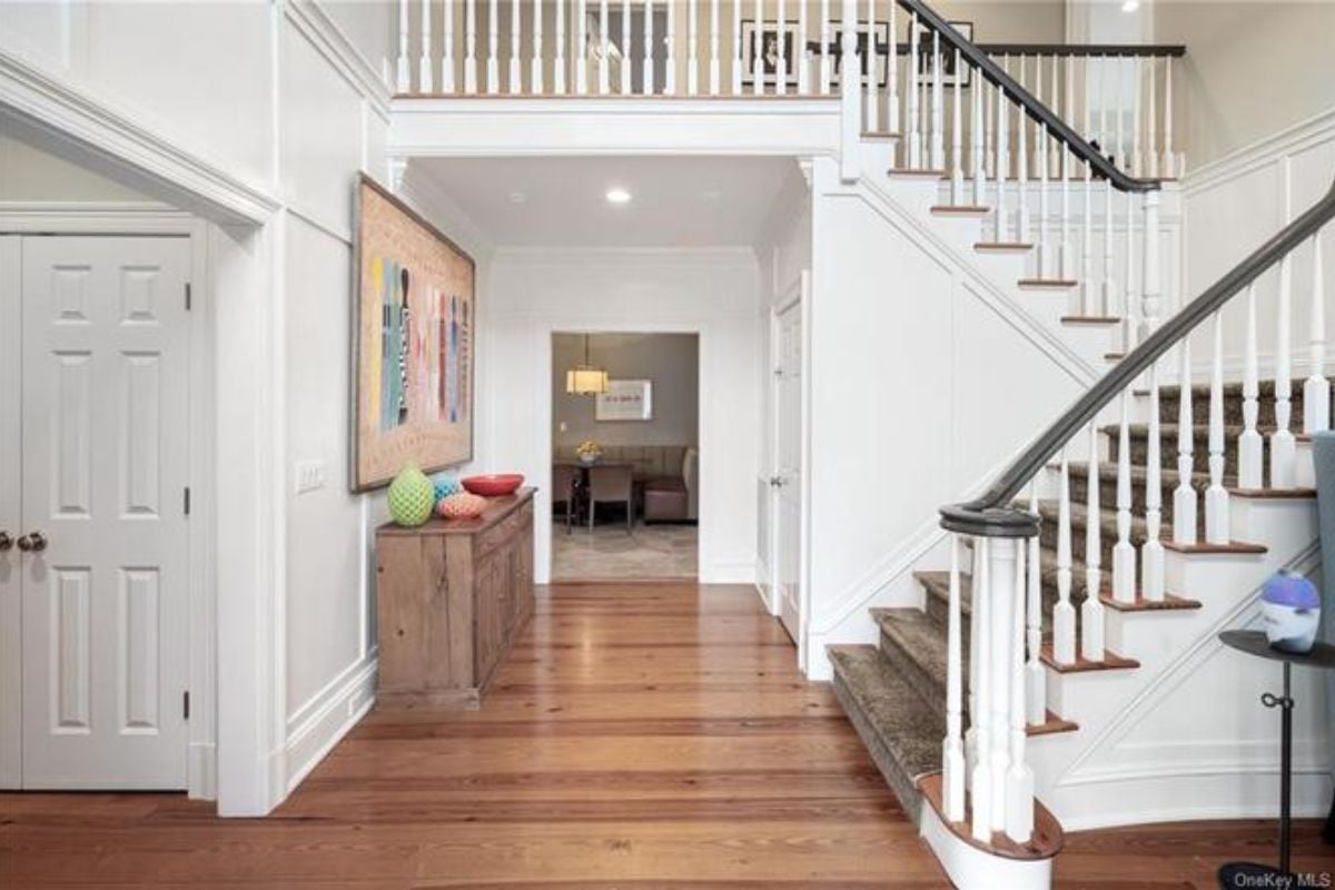 A foyer with a wooden floor, cabinet, and staircase.