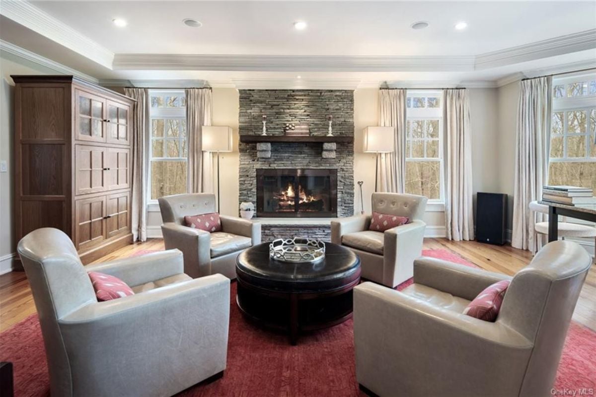 A living room with a fireplace, cabinet, windows, and a center table surrounded by chairs.