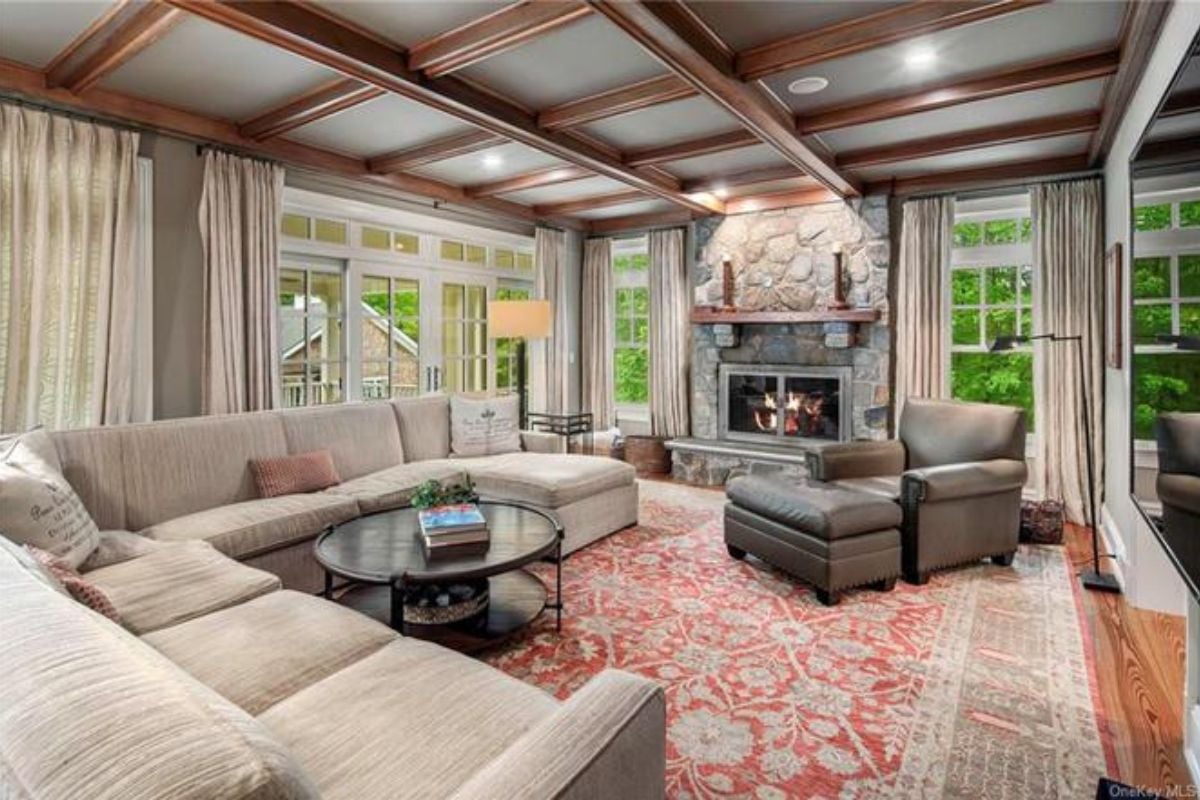A living room with a fireplace, exposed beam ceiling, windows, couches, and a center table.